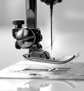 Close-up view of a sewing machine needle and presser foot in black and white, showcasing the intricate details of the metal components and thread in a professional and clean setting.