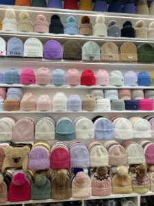 Showroom display of a wide assortment of winter hats and beanies, featuring colorful designs, pom-poms, and various knitting patterns, highlighting trendy and functional headwear options.