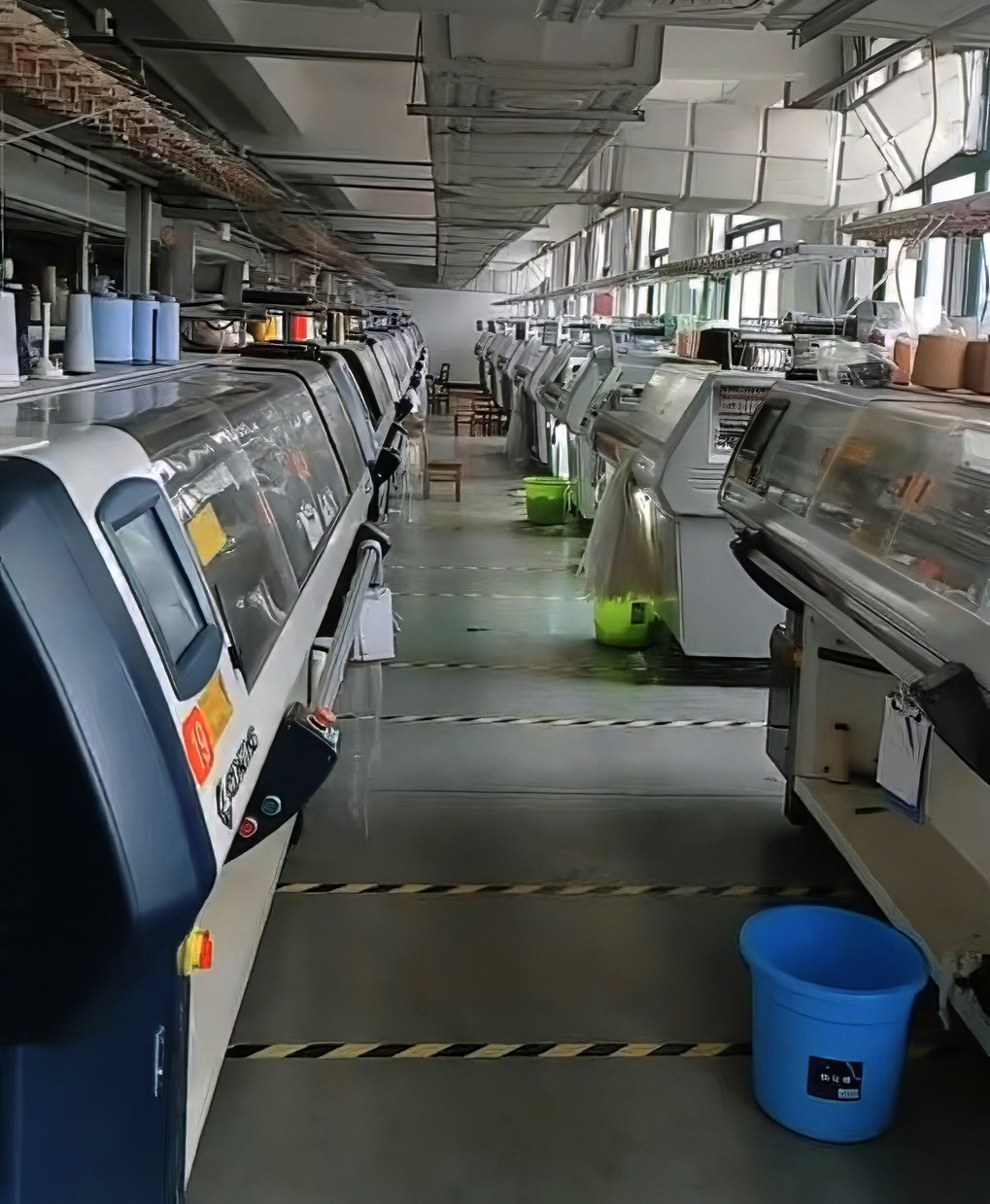 Interior of a modern knitting factory with rows of automated knitting machines, showcasing advanced textile production technology.