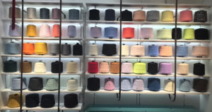 Display of colorful yarn cones arranged on shelves, featuring a wide variety of materials and shades for textile and knitting production.