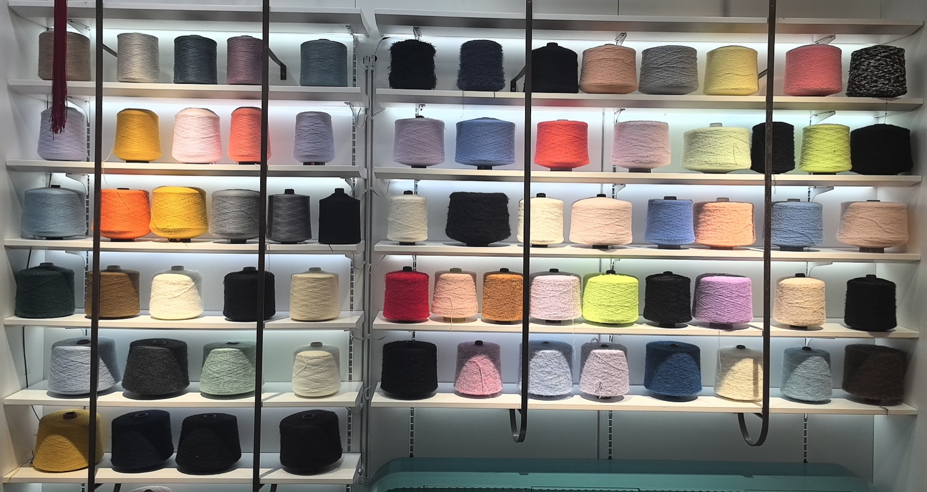 Display of colorful yarn cones arranged on shelves, featuring a wide variety of materials and shades for textile and knitting production.